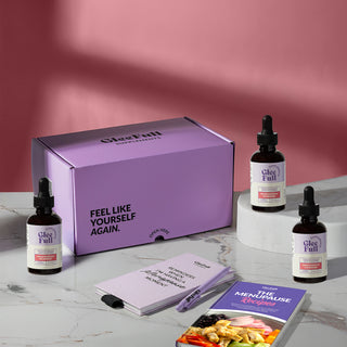Two hands against a light gray background — one squeezing a dark glass dropper, the other open palm beneath it to catch the liquid. Pink and purple headline text reads '1 Drop a Day to Melt Stubborn Fat, Crush Cravings & Boost Energy.' A purple circular badge reads 'How to Use: Shake well. Take 2 full vials (2 ml) in water, juice, or directly on your tongue each morning.'
