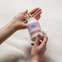 A person holds a white GleeFull Meno-Burn Collagen bottle with tan capsules in their open palm, against a soft cream blanket. Label reads 'Supports Stubborn Fat Burn, 60 Capsules'.